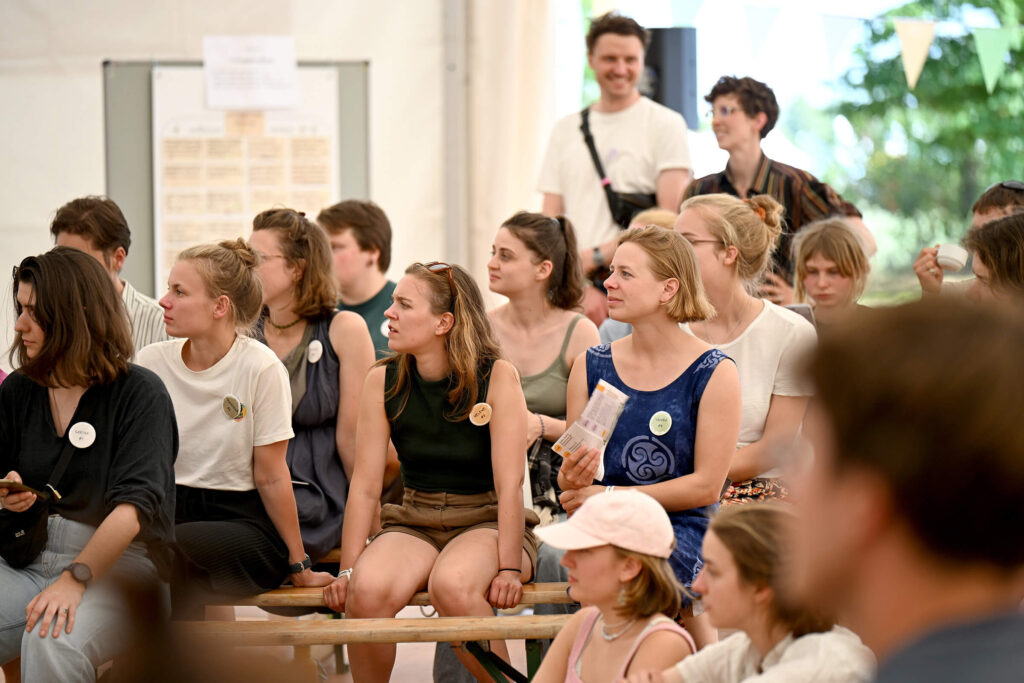 Hundert junge Menschen sitzen in einem Zelt und hören einem Referenten zu