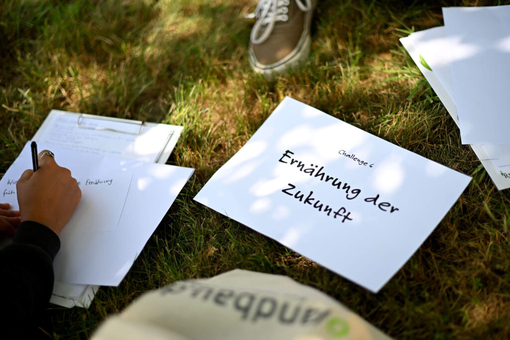 Papier mit dem Text „Challenge 6. Ernährung der Zukunft“ liegt auf einer Wiese