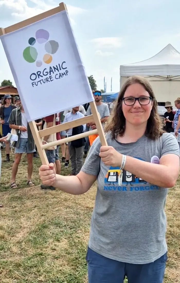 Jenny Eichelhard hält ein Schild mit dem Organic Future Camp Logo hoch.